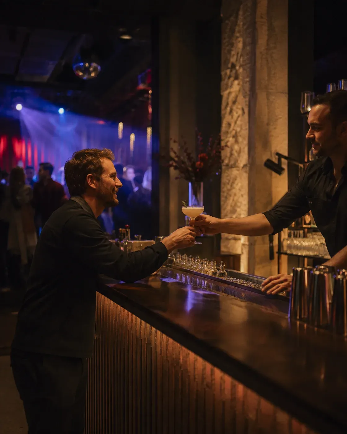 Illustrative Szene eines Barkeepers, der einem Gast in einem Nachtclub ein Getränk reicht; Tanzfläche und Bühnenlicht sind im Hintergrund zu sehen.