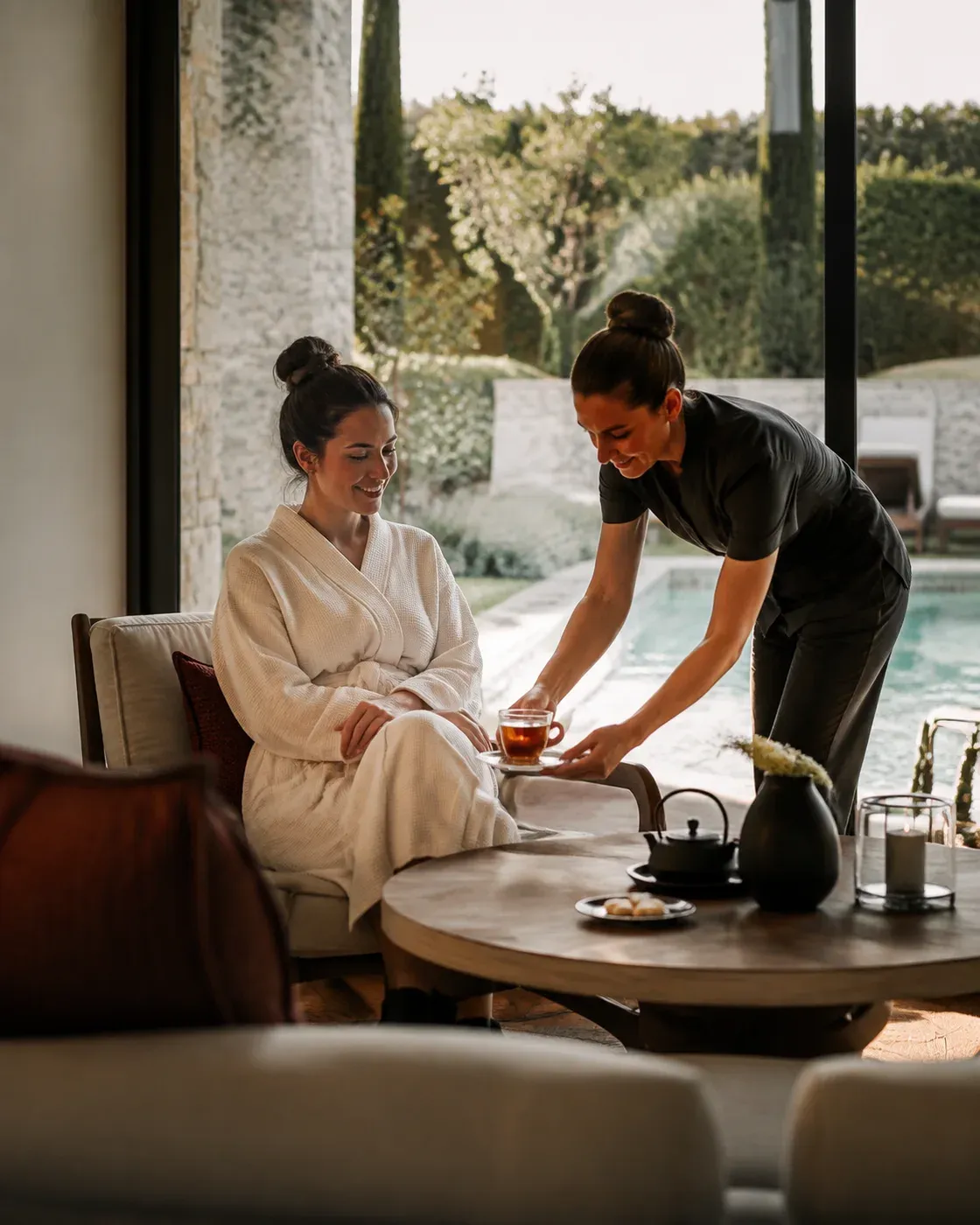 Illustratieve scène van een medewerker die thee brengt aan een gast in badjas in een rustige spa-lounge bij het zwembad.