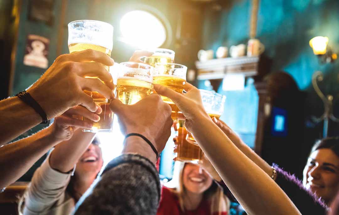 Een groep gasten proost met bier in een volle bar.